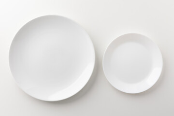 Two empty white plates are placed on a white table.