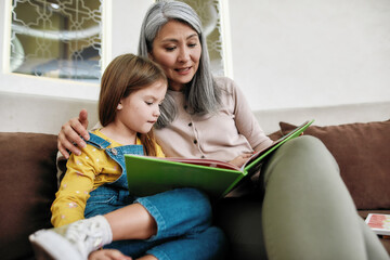 Happy grandmother reading book to granddaughter at home