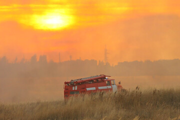 Naklejka premium Fire truck in a smoky field on sunset