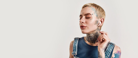 Listening to music. A close up of a white girl tattooed with piercing wearing denim overall...