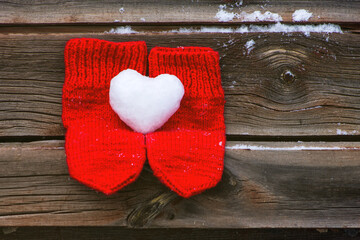 Red mittens with snow heart on old wooden surface background