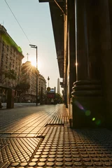 Foto op Plexiglas street canyon of Buenos Aires along a sidewalk at sunset with golden front light with a pillar in the foreground and an obelisk in the background © Jens