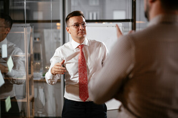 Business people in conference room use sticky notes on glass wall. Colleagues working on new project.
