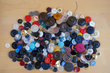   Many buttons of various colors and shapes lie in a heap on the table.