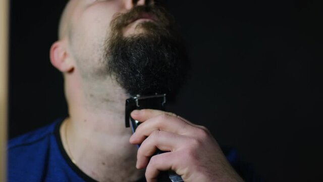 Bearded man shaves with a trimmer, close-up
