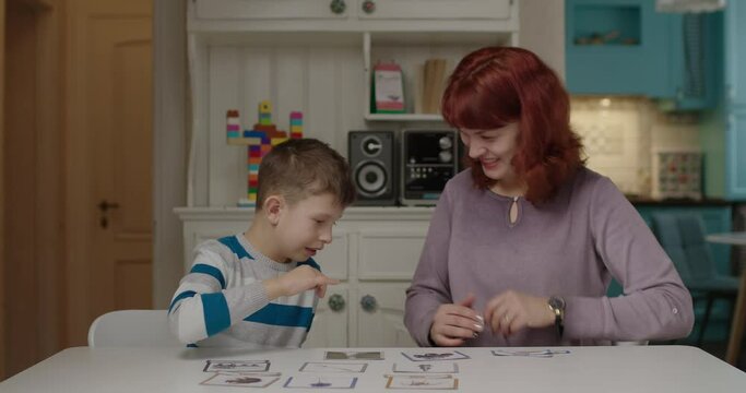 Autism therapist working with kid with autism to practice skills in reading. School boy with autism learning with mother at home. Autistic child matching words with pictures.