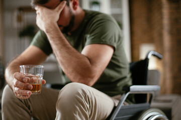 Depression man in wheelchair drinking alcohol at home. Lonely man is addicted of alcohol.