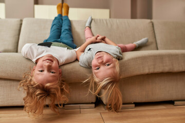 Have fun. Portrait of playful kids, little boy and girl lying upside down on a sofa in the living...