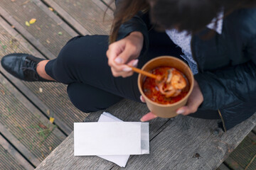 White envelope mockup. The girl on the bench eats soup with seafood shrimp.