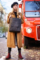 Foto op Plexiglas Blonde girl in trench and beret on the city street with red bus background. Young female holding black bag. Fashion or London travel concept © boytsov