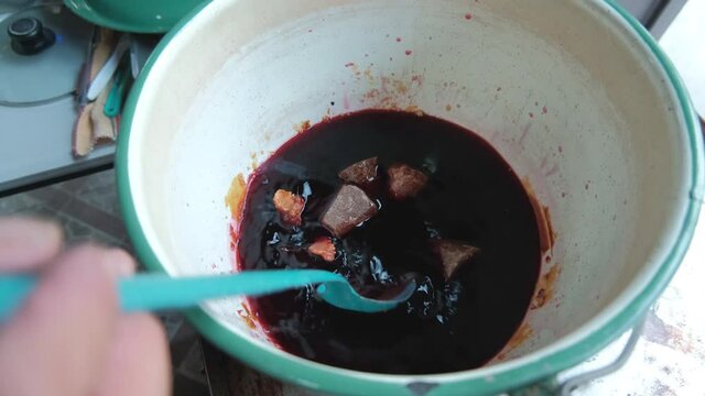 Hand adding brown sugar canes to a tall saucepan with punch