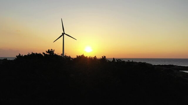 Drone video showing red sunset and windmills and trees and sea