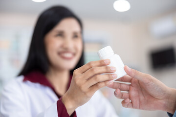 Asian Female pharmacist holding medicine white bottle giving advice to customer in chemist shop or pharmacy Thailand close up and selective focus