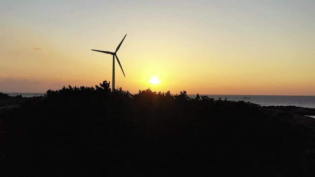 Drone video showing red sunset and windmills and trees and sea