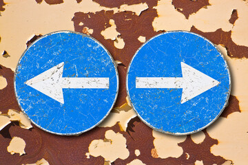 Old blue metallic arrow sign indicating to go left and right against an aged rusty metal wall -...