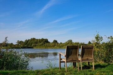 relaxation scenery, two chairs invites to take a rest next to pond at summer and blue sky