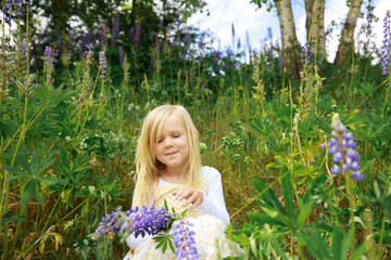 Beautiful little blonde girl posing with lupines in the forest.