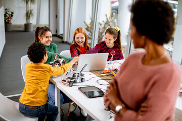 Happy kids with their African American female science teacher with laptop programming electric toys and robots at robotics classroom