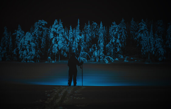 Female hiker wearing snow shoes, walking across a snow covered tundra in a wild winter landscape at night.