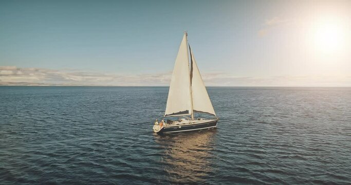 Sailing yacht race at sun light aerial. Yachting on serene seascape at open sea. Boat with big white spinnaker sail at ocean bay. Lonely ship cruise at water on summer sunny day. Cinematic drone shot