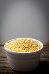 Dry millet in white ceramic bowl on old wooden table with copy space.