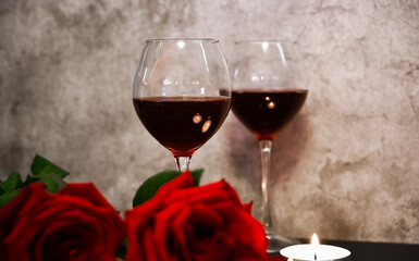 Two glasses of red wine, red roses and candles on cement background. St. Valentine's theme
