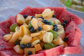 Plate with raw sliced fruits on a table - blueberries, melon, watermelon, banana, grapes, healthy snacks, party concept, appetizers for celebration, nutritious food