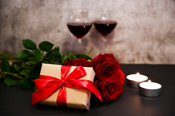 A gift with rose,candles and awo glasses of red wine on cement background. St. Valentine's theme