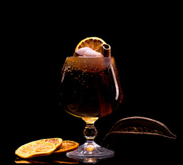 Cocktail with ice, lemon and cinnamon stick in a glass on a black background close-up