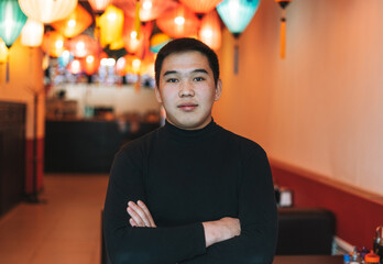 Handsome young asian man in black clothes in festive chinese vietnamese restaurant colorful paper lanterns, small own business