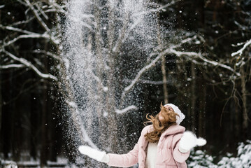 Fototapeta na wymiar a funny live photo of a girl in a winter park who throws snow in front of her
