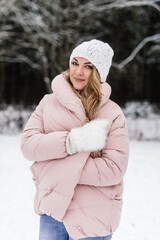 young beautiful woman wraps herself in a warm jacket in a snowy park