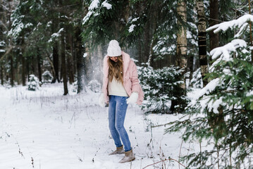 young beautiful woman is walking among the snowy fir trees and snow is falling on her