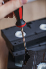 A man takes apart an old videotape and uses a screwdriver to unscrew the bolts from the case. Old technologies.