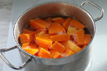 Pieces of red pumpkin are cooked in a pan on an induction hob.
