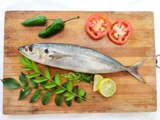 Fresh Round Scad Fish decorated with herbs and vegetables on a wooden pad, White Background.Selective Focus.