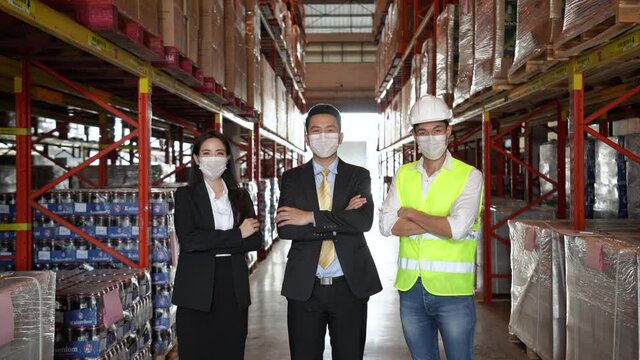 Group of Asian business people and warehouse worker wear protective face mask during working in distribution warehouse due to covid-19 pandemic crisis. Global business and logistic industrial concept.