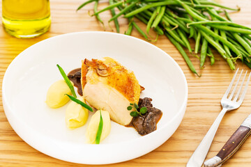 Roasted chicken breast with mashed potatoes, green beans and mushroom sauce aside a fork, a folding knife, olive oil and a pile natural green beans on an oak wood table.