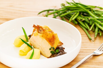 Roasted chicken breast with mashed potatoes, green beans and mushroom sauce aside a fork and some natural green beans on an oak wood table.