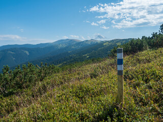 sign pole with tourist mark at ridge of Low Tatras mountains, hiking trail with mountain meadow, scrub pine and grassy green hills and slopes. Slovakia, summer sunny day, blue sky background © Kristyna