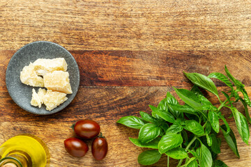 Fototapeta na wymiar Italian cuisine ingredients: basil, tomatoes, olive oil and parmesan cheese on a vintage wood chopping board. Flat lay, top view with copy space.