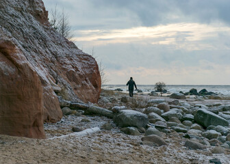 sandstone cliff. human silhouette by the sea, Wild beach Baltic coast in December. Vidzeme rocky seashore - obrazy, fototapety, plakaty