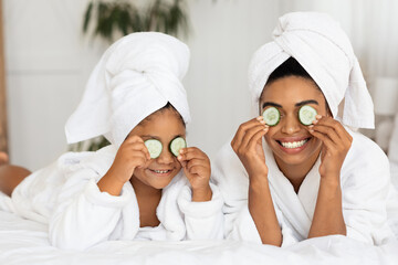 Funny Black Mom And Daughter In Bathrobes With Cucumber Slices On Eyes