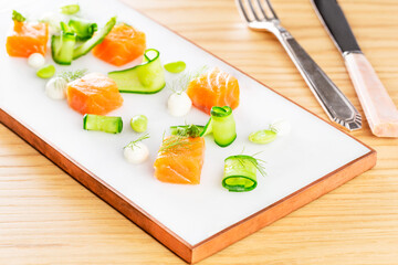 Dices of raw salmon with asparagus, edamame beans, cream cheese and zucchini on a marble plate aside a set of silver cutlery on a wood background.