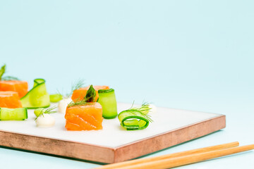 Dices of raw salmon with asparagus, edamame beans, cream cheese and zucchini on a marble plate aside a pair of chopstick over an infinite blue background with copy space.