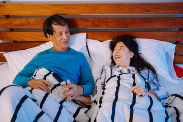 Romantic senior couple holding hands on a bed at night.