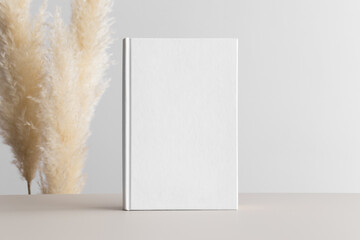 White book mockup with pampas decoration on a beige table.