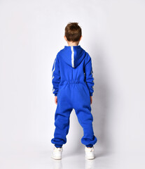 Full length rear view of a little preschooler or schoolboy in a warm blue sports suit with a hood and white sneakers. Isolated on gray background with copy space. Sports fashion for children.