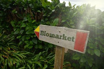 vintage old wooden signboard with text biomarket near the green plants.