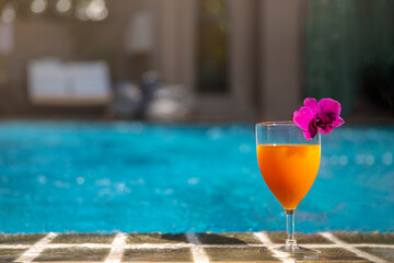 Glass of Orange juice with purple orchid  on on the pool  at outdoor swimming pool, summer tropical holiday concept